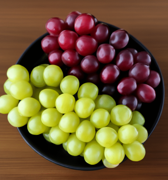 High-resolution digital photograph showcasing a black round ceramic bowl filled with clusters of white grapes and red grapes on a wooden surface.
