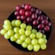 High-res photo of black ceramic bowl with white grapes and red grapes on wooden surface, highlighting texture and vibrant colors.
