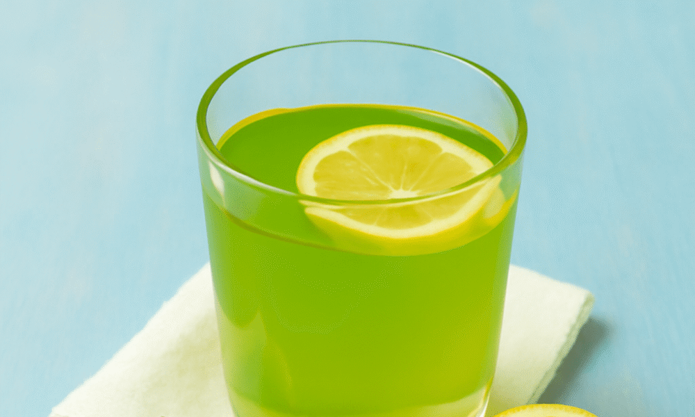 A refreshing glass of lemon-infused green drink with a slice of lemon, fresh basil, and a linen napkin on a soft blue wooden surface. Lemon Balm Recipe for Weight Loss.