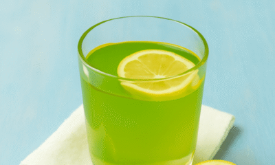 A refreshing glass of lemon-infused green drink with a slice of lemon, fresh basil, and a linen napkin on a soft blue wooden surface. Lemon Balm Recipe for Weight Loss.