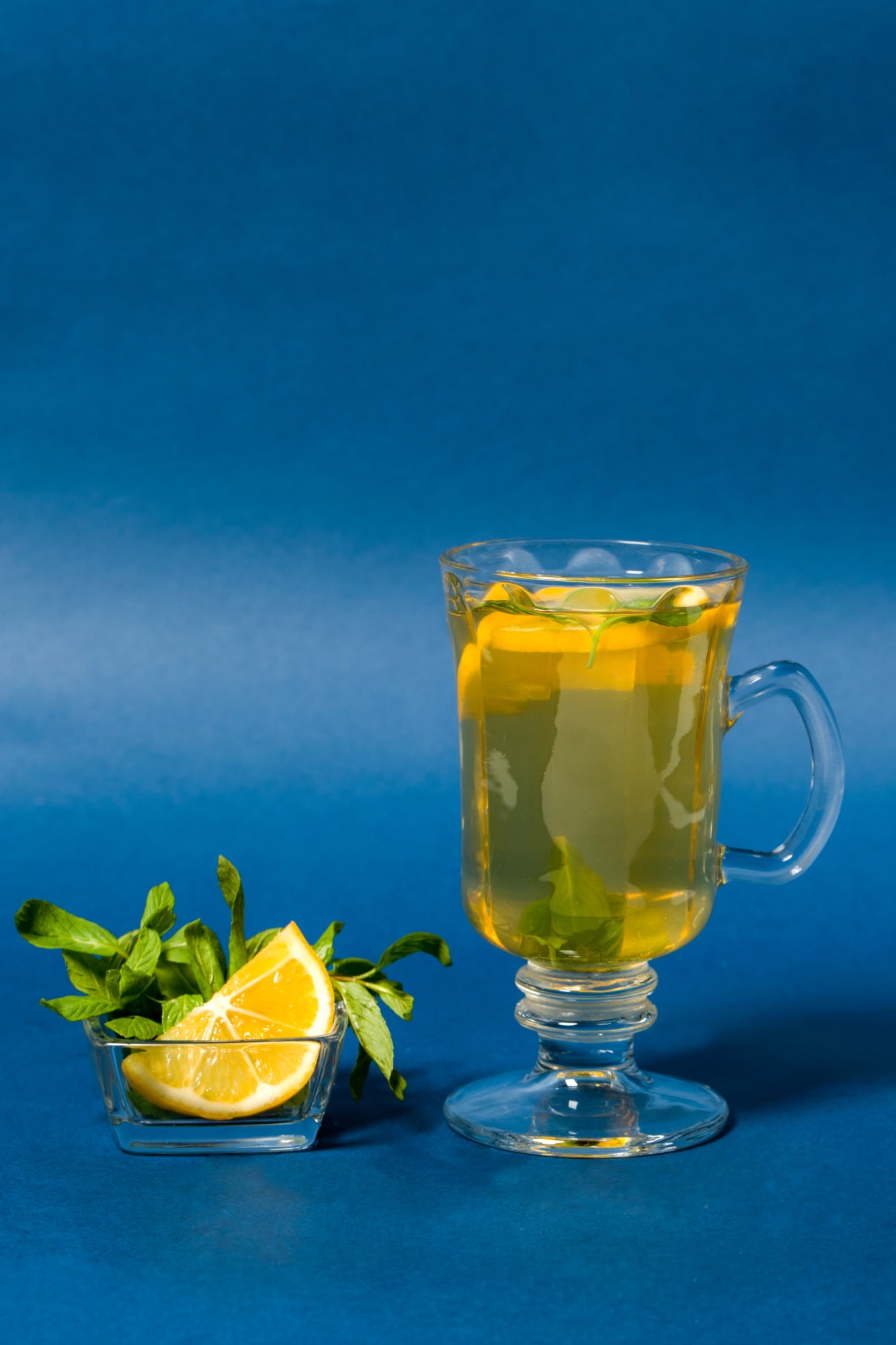 Lemon Balm benefits shown in a glass of herbal tea with lemon slices and mint leaves, styled on a blue background for a wellness vibe.