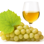 A White grape glass filled with amber-colored wine, accompanied by a bunch of plump green grapes and a vibrant grape leaf, set against a clean white background.