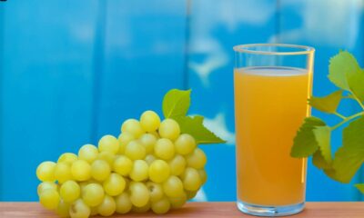 White grape juice in a glass with green grapes and leaf on white background, highlighting freshness and natural taste.