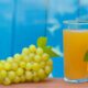 White grape juice in a glass with green grapes and leaf on white background, highlighting freshness and natural taste.