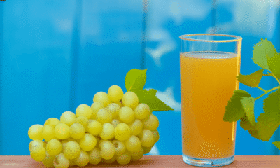 A White grape glass filled with amber-colored wine, accompanied by a bunch of plump green grapes and a vibrant grape leaf, set against a clean white background.