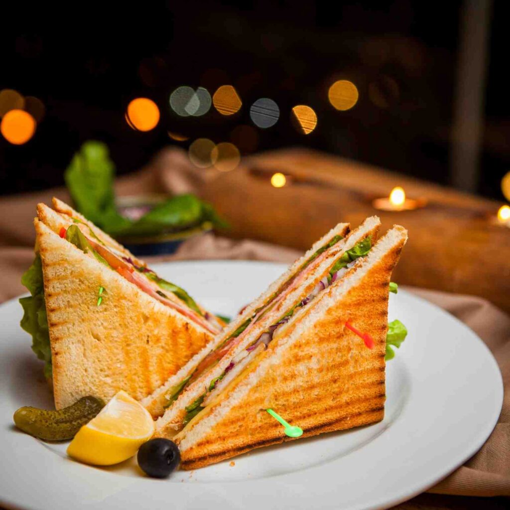 Grilled chicken sandwiches with fresh vegetables, served with lemon, olives, and pickles on a white plate healthiest fast food meals.