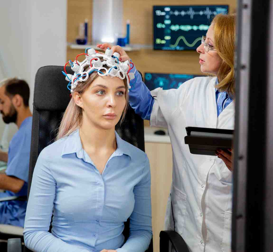 Neuropsychological testing in progress with an EEG cap being adjusted by a doctor, displaying brain analysis data on screen.