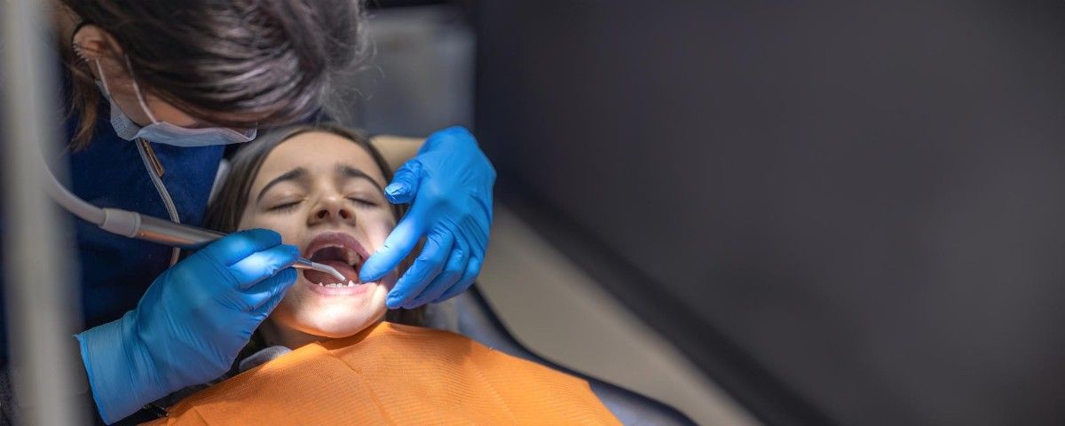 Dentist performing cavity filling on a young patient lying in dental chair, using tools and wearing gloves and mask for How Long Does It Take to Fill a Cavity?