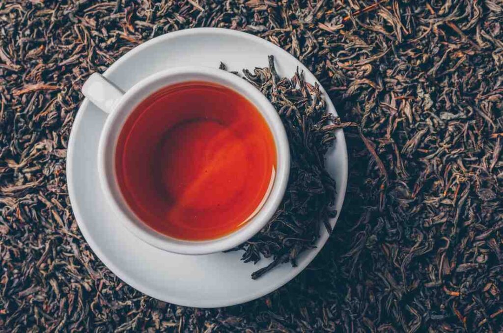 Cup of hot black tea on a white saucer surrounded by loose black tea leaves, showcasing rich color and flavor of Black Tea vs Green Tea